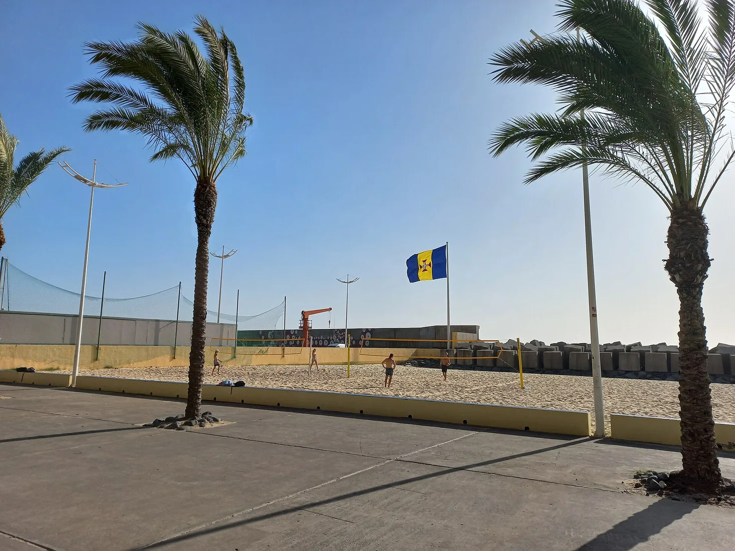 Concrete breakwater blocks and the Madeira flag at the edge of Calheta's beach