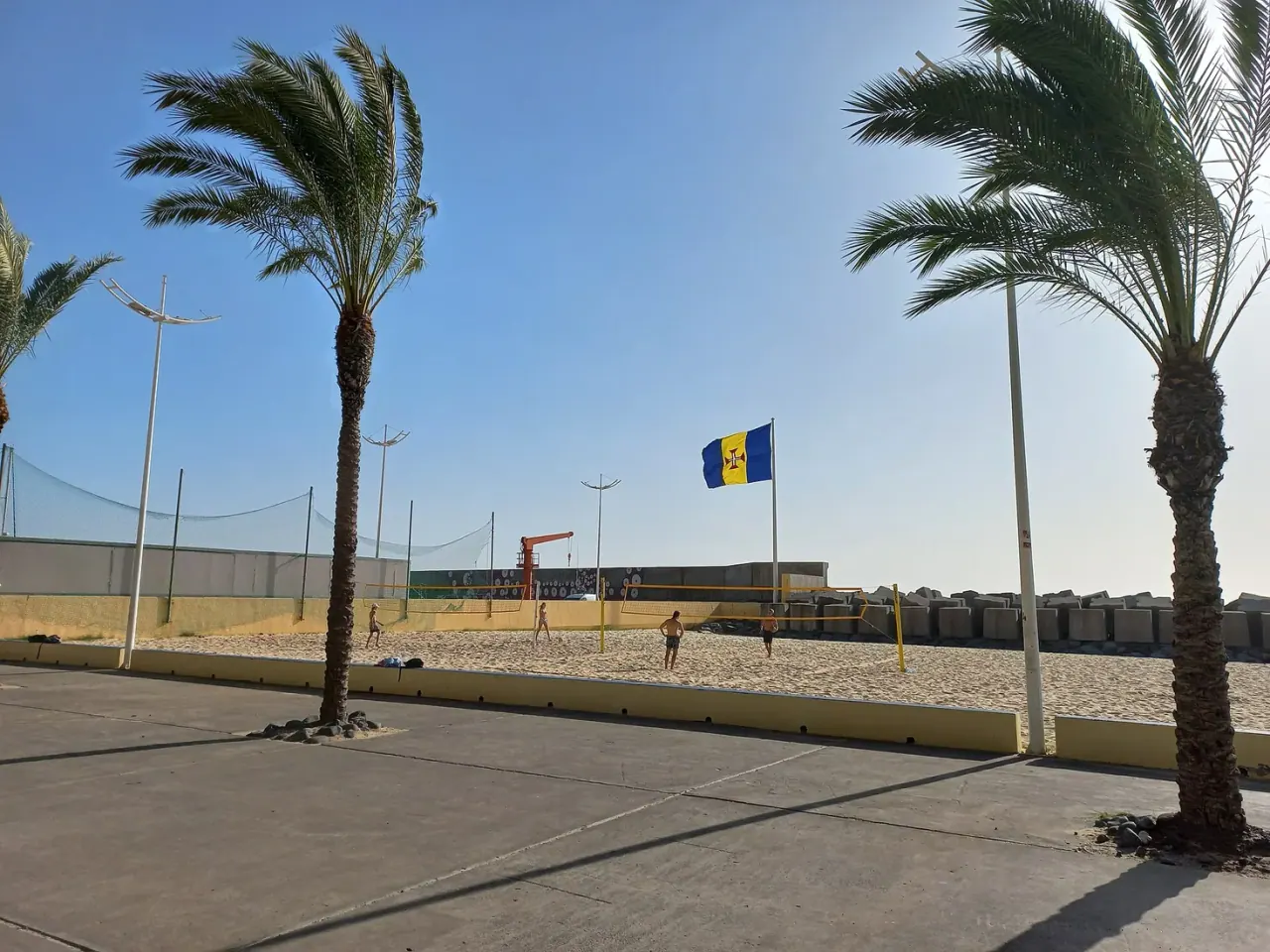 Concrete breakwater blocks and the Madeira flag at the edge of Calheta's beach